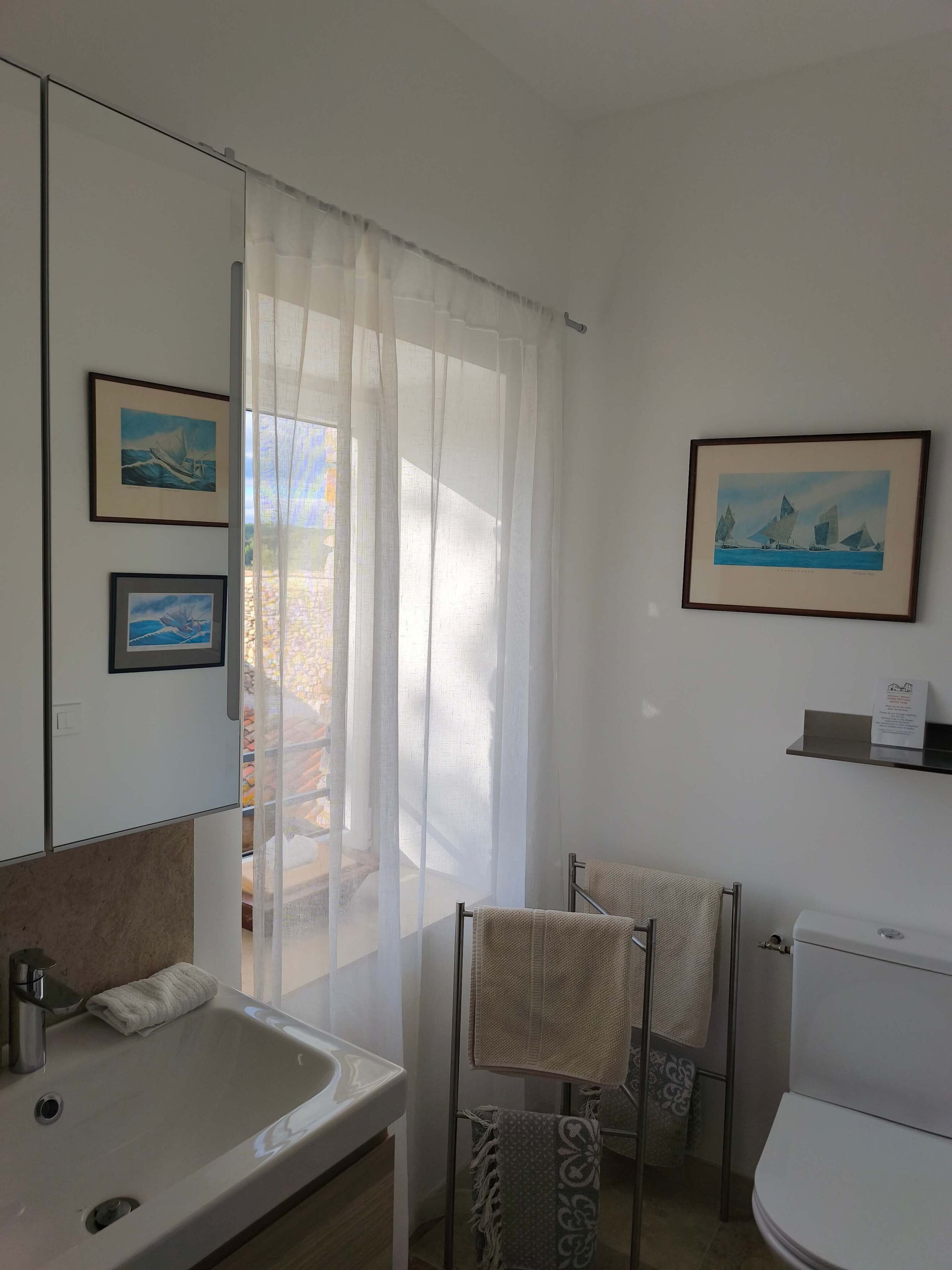Kylpyhuoneessa on valkoinen pesuallas, wc ja suihkutila. Seinällä on kaksi kehystettyä kuvaa, toisessa on purjevene ja toisessa purjevene vuoristomaisemassa.