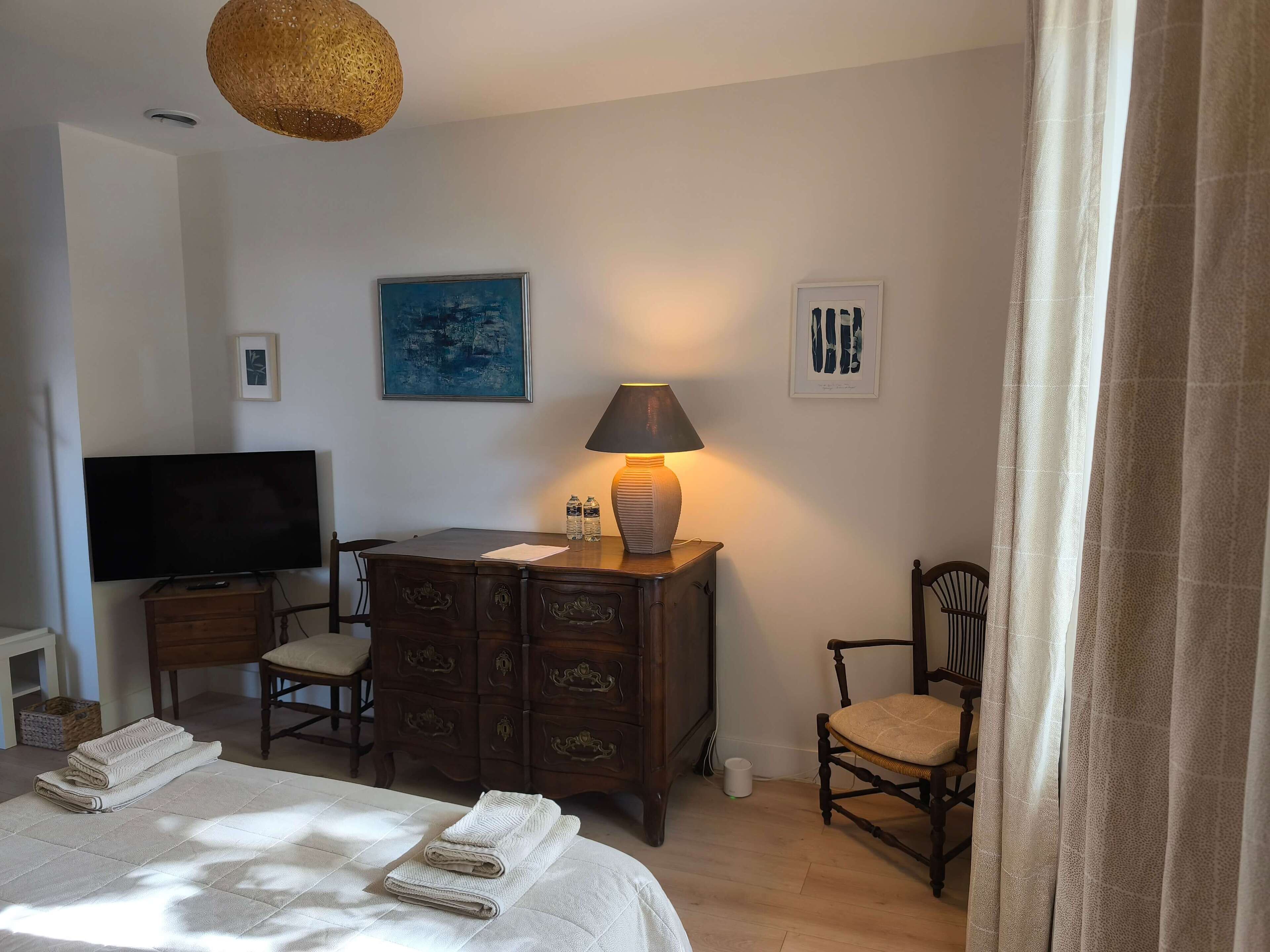 Une chambre d’hôtel équipée d’un lit, d’une télévision, d’une commode, d’une chaise et d’œuvres d’art accrochées aux murs.