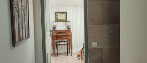 A hallway leading to a dining area with a wooden table and chairs, a framed picture on the wall, and a cat on the floor.