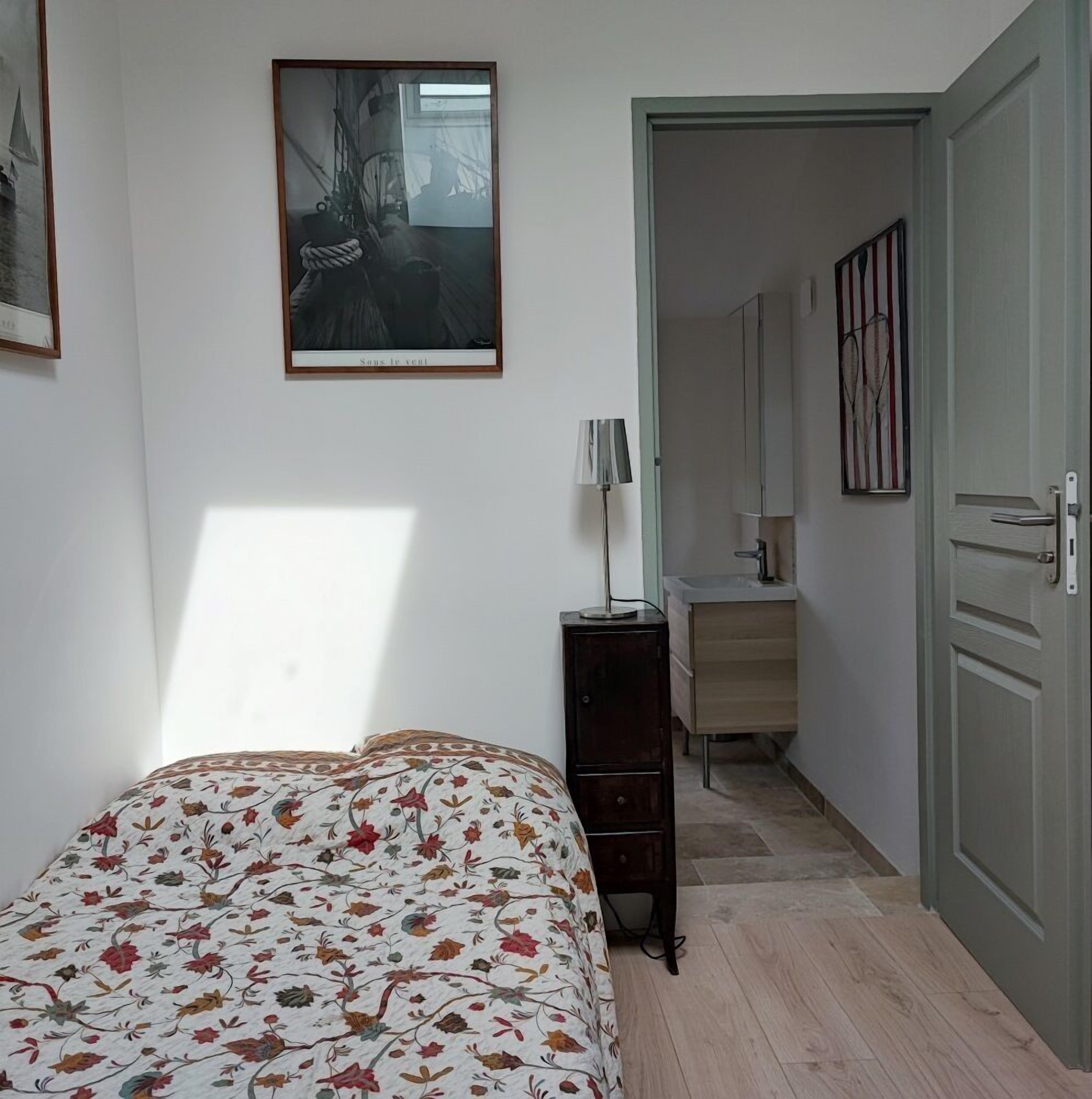A bedroom with a bed, a dresser, a desk, and a door leading to a bathroom.