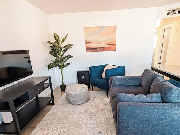 A living room with a flat-screen TV, a potted plant, a blue sofa, and a painting on the wall. - Simple Mesa 2nd Floor 2 Bedroom Unit (Mesa)