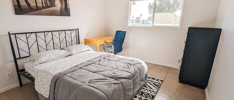 A bedroom with a bed, a desk, a chair, a window, and a door.