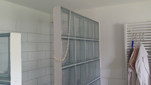 A bathroom with a glass shower enclosure, a towel rack with towels, and a white tiled wall. - Vacation apartment Ludwigshöhe (Weißenburg)