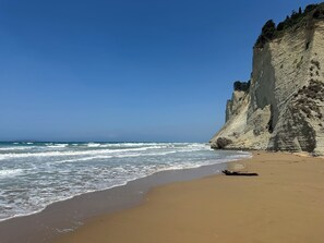 A beach with a sandy shore and a rocky cliff. - Villa Avra Arillas : Vue sur mer et coucher de soleil avec très grande piscine (Arillas Magouladon)