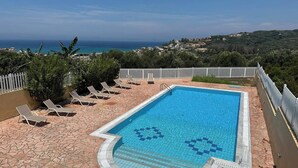 A rectangular pool with a tiled border, surrounded by lounge chairs and a white fence.