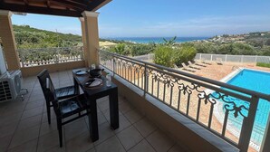 A balcony with a table and chairs, overlooking a swimming pool and a scenic view of the coastline.