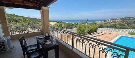 A balcony with a table and chairs, overlooking a swimming pool and a scenic view of the coastline.