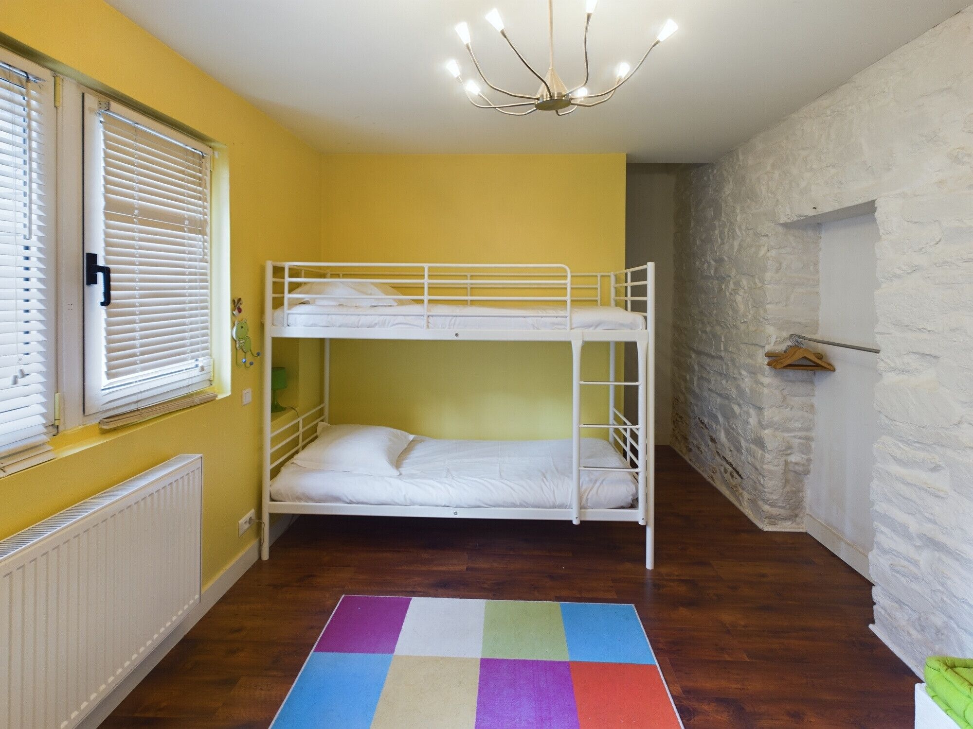 A bunk bed room with a radiator, a colorful rug, and a stone wall.
