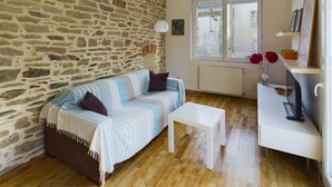 A cozy living room with a stone wall, a striped sofa, a white coffee table, and a TV on a white stand. - -STONE-Maison de Ville à Concarneau (Concarneau)