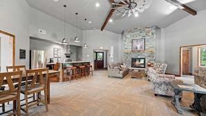 A spacious living area with a stone fireplace, wooden furniture, and a kitchen with a bar. - Cabin · Hot Tub · Arcade · Trails · Sleeps 16 (Lead)