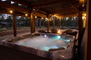 A hot tub under a wooden pergola with string lights, surrounded by wicker chairs. - Cabin · Hot Tub · Arcade · Trails · Sleeps 16 (Lead)