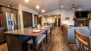 A modern kitchen with a central island, dark wood cabinets, stainless steel appliances, and a dining area with a long table. - Cabin · Hot Tub · Arcade · Trails · Sleeps 16 (Lead)
