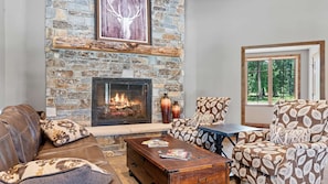 Une cheminée en pierre, un canapé en cuir, un fauteuil à motifs et une table avec des magazines.