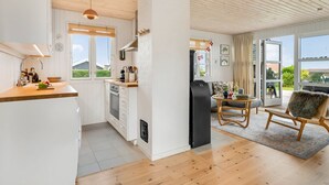 A modern kitchen with white cabinets, a wooden countertop, and a built-in oven. There is a dining area with a wooden table and chairs, and a large window offering a view of the outdoors.