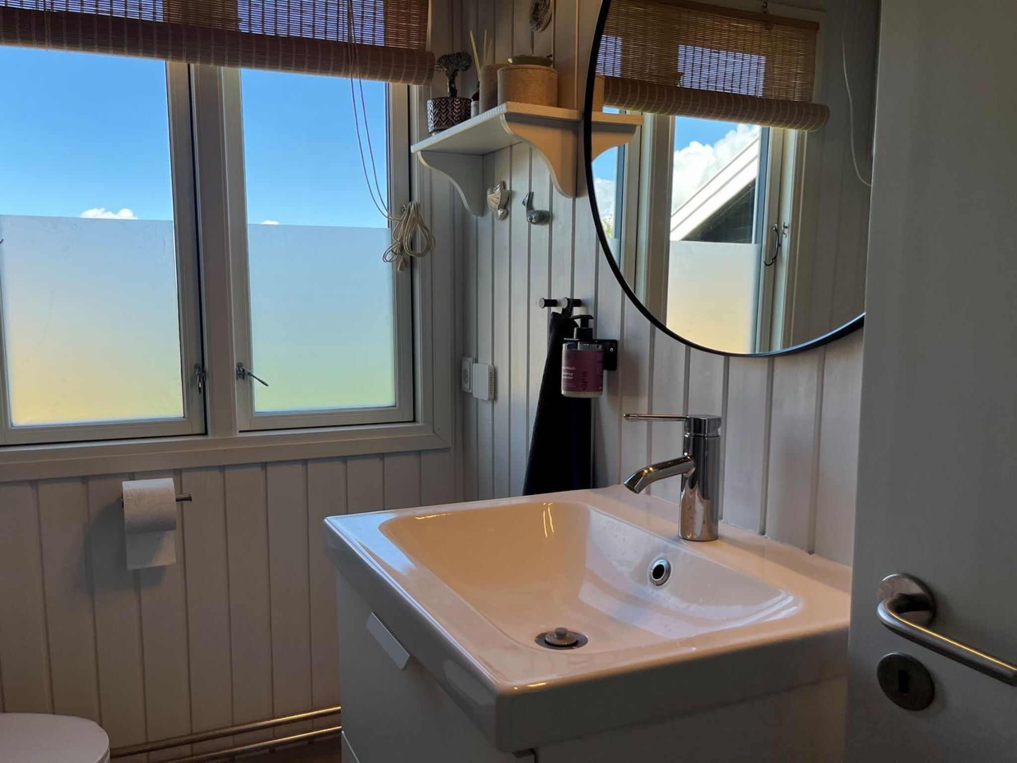 A bathroom with a white sink, a mirror, a window, and a towel rack.
