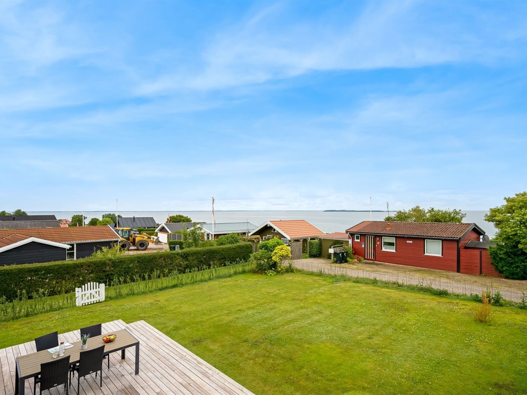 A residential area with houses, a grassy yard, and a wooden deck with chairs and a table.