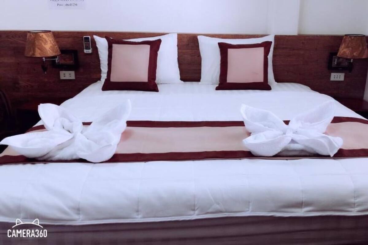 A neatly made bed with white and brown bedding, two pillows, and a decorative bow.