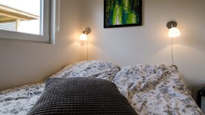 Un lit avec une literie à motifs floraux, un plaid épais de couleur sombre et deux lampes fixées au mur.
