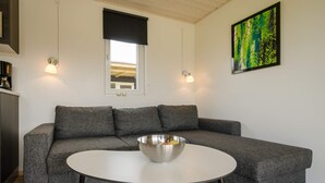 Un salon moderne avec un canapé d’angle gris, une table ronde blanche et un tableau accroché au mur.