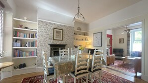 A dining area with a table set for four, surrounded by white chairs, a patterned rug, and a bookshelf filled with books.