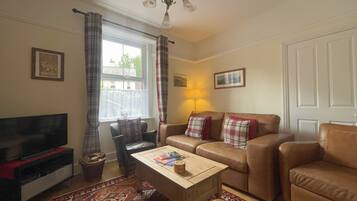 A living room with a sofa, armchair, coffee table, TV, and a patterned rug.