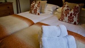 A neatly made bed with white and brown linens, a wooden nightstand with a lamp, and a floral-patterned wall.