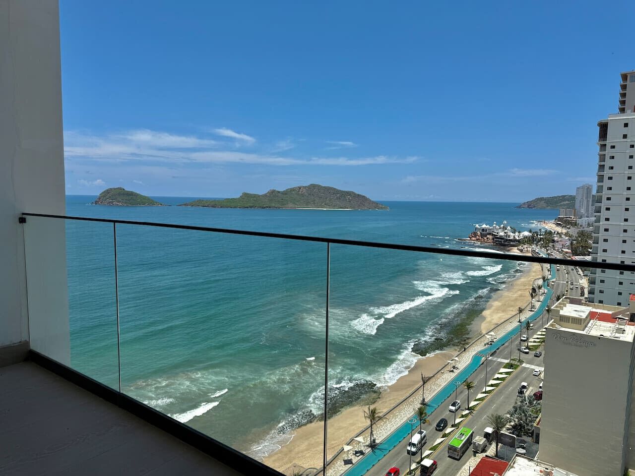 A balcony with a view of the beach and ocean, a road with vehicles, and a building with the name "Dom Pedro" on it.