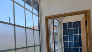 Ein Korridor mit einem großen Fenster links und einem kleineren Fenster rechts, der zu einem Raum mit Holzboden und einem kleinen Tisch führt.
