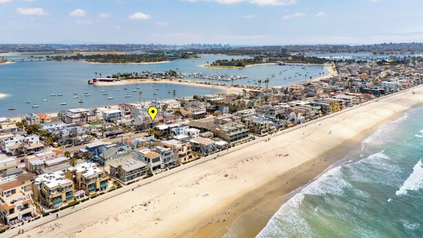 An aerial view of a coastal town with a beach, marina, and residential buildings.