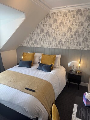 A hotel room with a large bed, a nightstand with a lamp, and a window with a view of trees.
