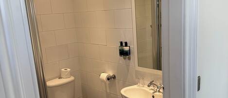A small, modern bathroom with white tiles, a toilet, a sink, and a mirror.