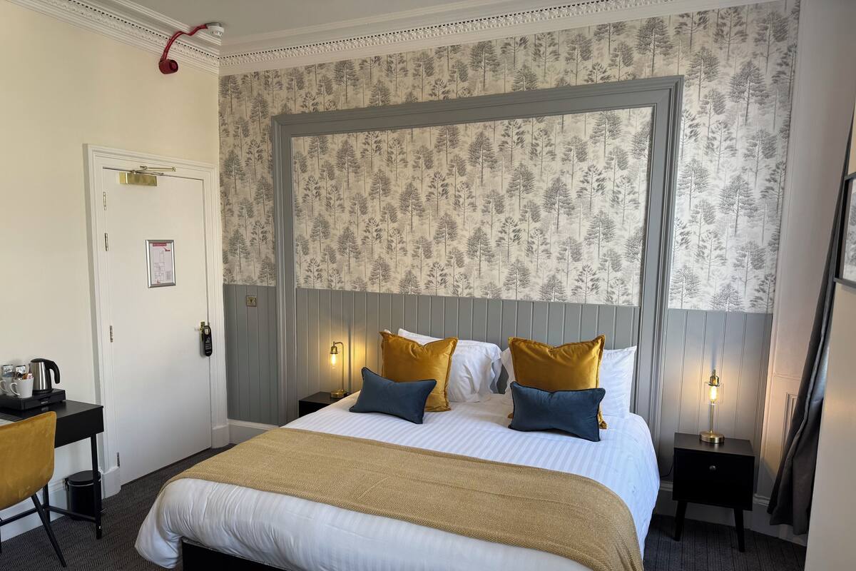 A neatly arranged hotel room with a large bed, two bedside tables, a desk, and a chair.