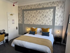 A neatly arranged hotel room with a large bed, two bedside tables, a desk, and a chair.