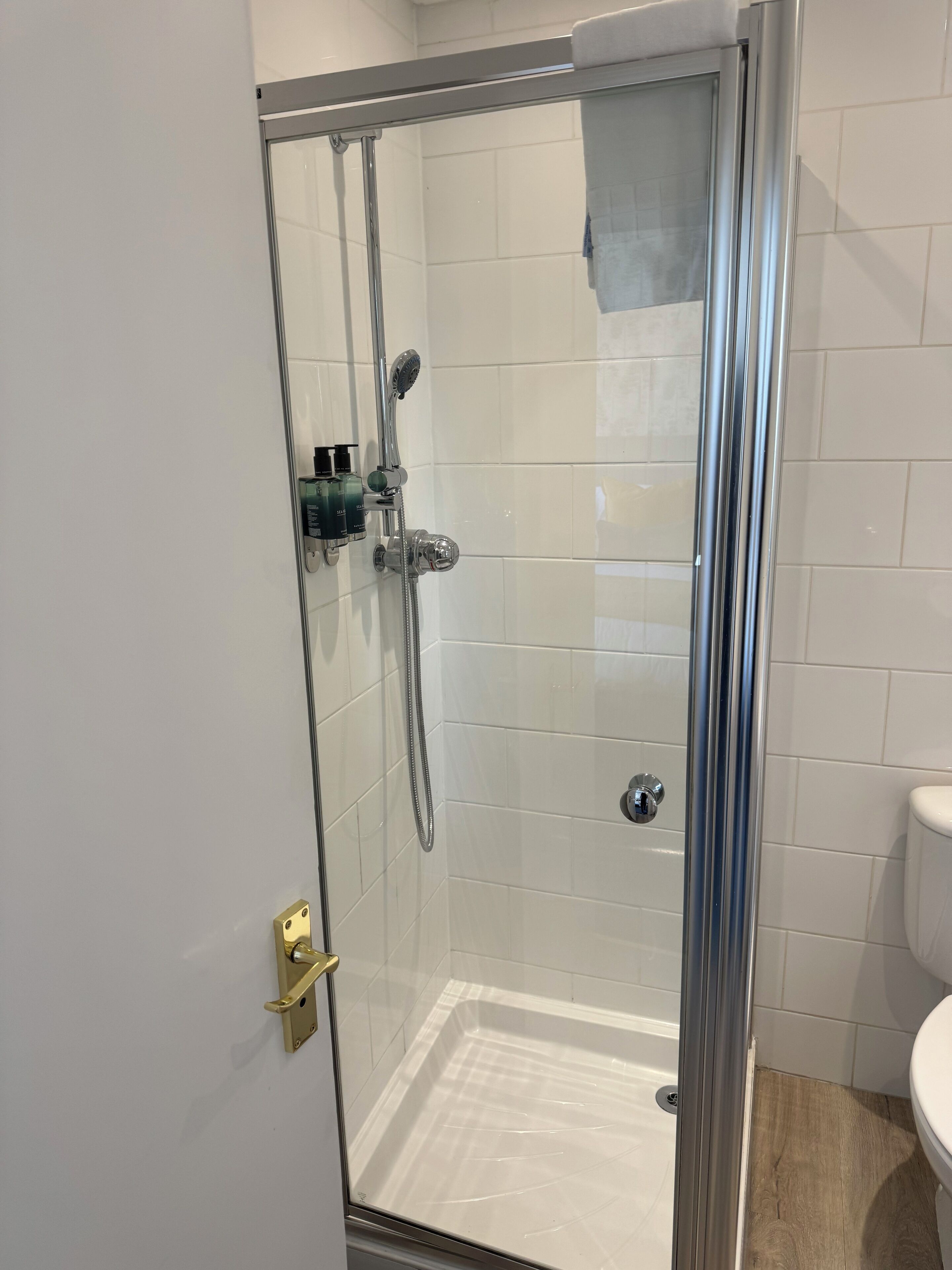 A glass-enclosed shower with a chrome frame, a handheld showerhead, and a wall-mounted control panel.