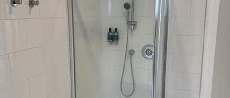 A glass-enclosed shower with a handheld showerhead and a wall-mounted faucet.