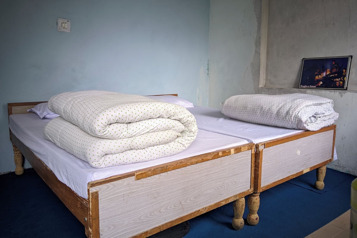 Una habitación con dos camas de madera, cada una con un colchón blanco y una manta de lunares.