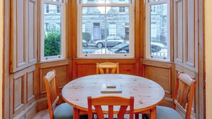 A corner room with a bay window, wooden paneled walls, a round wooden table with chairs, and a view of the street outside. - beautiful- spacious ground floor newington flat (edinburgh)