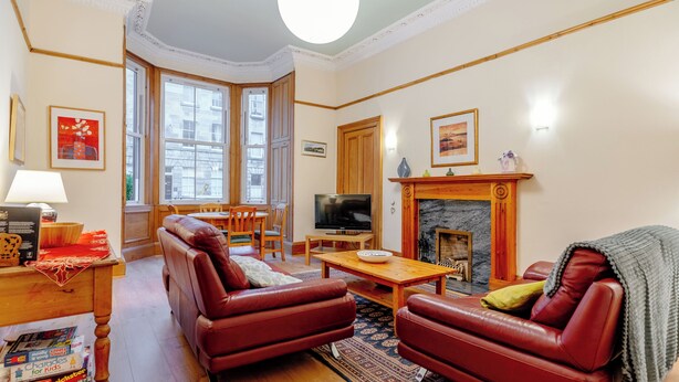 A living room with a fireplace, leather sofas, a wooden coffee table, and a television. - beautiful- spacious ground floor newington flat (edinburgh)