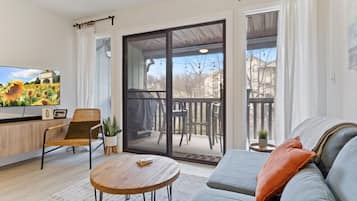 A modern living room with a sofa, a wooden coffee table, a TV, and a sliding glass door leading to an outdoor deck.
