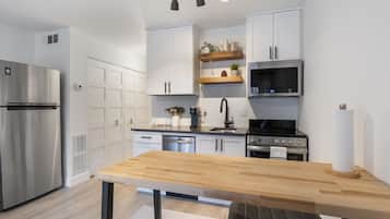 A modern kitchen with white cabinets, stainless steel appliances, a wooden table, and a black countertop.