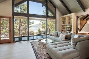 A spacious living room with a large window, a sofa, a coffee table, and a bookshelf. - Sunset Spectacular (Big Bear Lake)