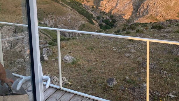 A wooden deck with a glass railing overlooking a mountainous landscape.