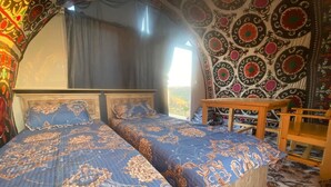 A room with two beds, a wooden table, and a view of the outdoors.