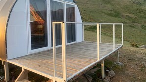 A dome-shaped cabin with a wooden deck and large windows, set against a hilly landscape.