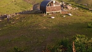 A single-story building with a curved roof, situated on a grassy hillside with a backdrop of rolling hills.
