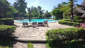 A pool area with stone flooring, benches, and palm trees. - 2-bed apartment Malindi Kenya Direct beach location (Malindi)