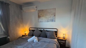 Un lit bien fait, avec une serviette pliée, deux lampes de chevet, un climatiseur fixé au mur et un tableau au-dessus du lit.