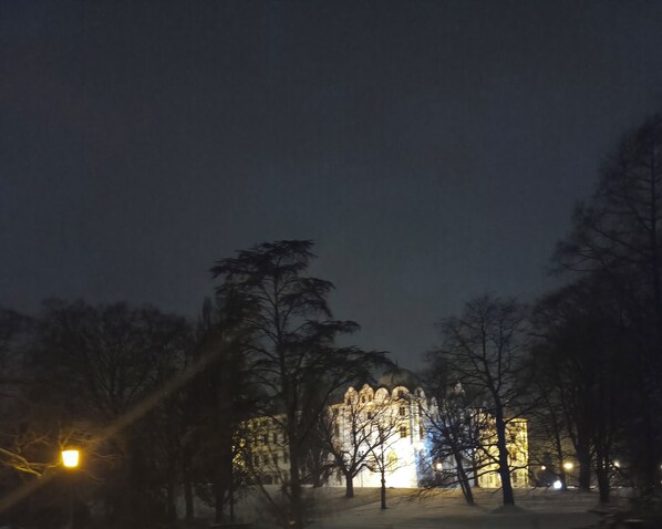 Ein Gebäude mit beleuchteten Fenstern und einem mit Schnee bedeckten Untergrund, umgeben von kahlen Bäumen.