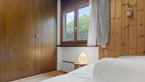 Un dormitorio con paredes de madera, una ventana con cortinas, una cama y una mesita de noche con una lámpara.