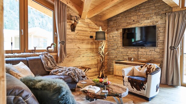 A cozy log cabin interior with a stone wall, wooden ceiling beams, a large TV, and a fireplace. - Chalet Lessner - Pure Design & Tranquility (Leutasch)